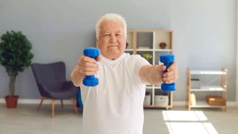 Activité Physique Adaptée (APA) à domicile. Patient qui réalise un exercice de renforcement musculaire avec haltères.